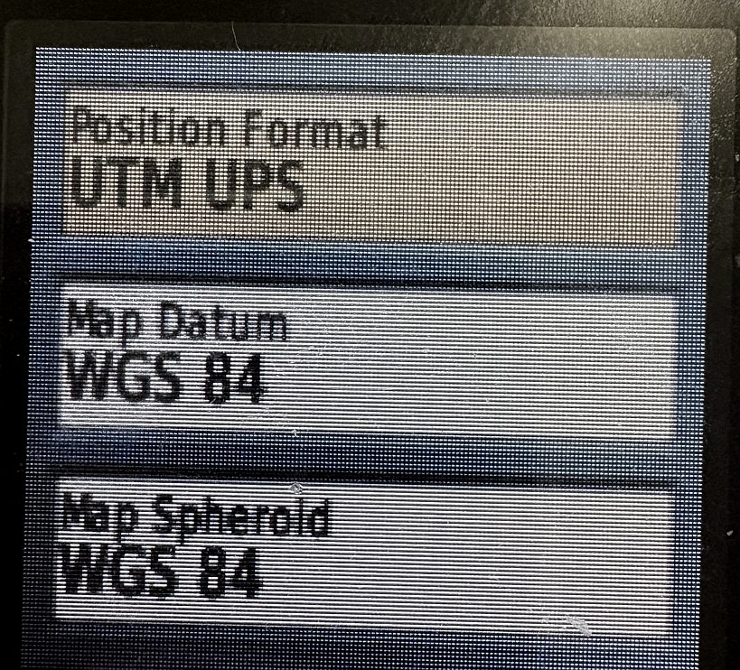 The Position Format setup screen on a Garmin GPSMAP 64st, showing Position Format set to UTM UPS, Map Datum WGS 84 and Map Spheroid WGS 84.